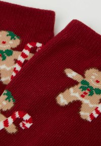 Røde strikkede sokker med et peberkagemandmotiv med grønne accenter, kombineret med røde og hvide stribede sukkerrør. Blød tekstur.