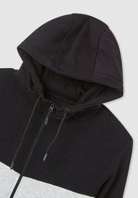Felpa con zip nera e grigia con cappuccio, caratterizzata da un design bicolore, texture liscia e blocchi di colore a contrasto. Stringhe regolabili.