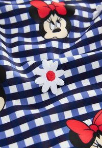 Granatowa tkanina w kratkę gingham z grafiką Minni Mouse i czerwonymi kokardkami. Wzór uzupełnia haftowana biała stokrotka z czerwonym środkiem.