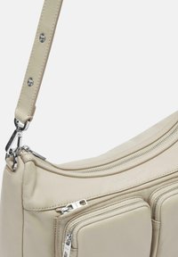 Borsa a spalla in cuero beige con più tasche con zip, texture liscia e accessori in tonalità argento. Tracolla regolabile con dettagli a bottone a pressione.