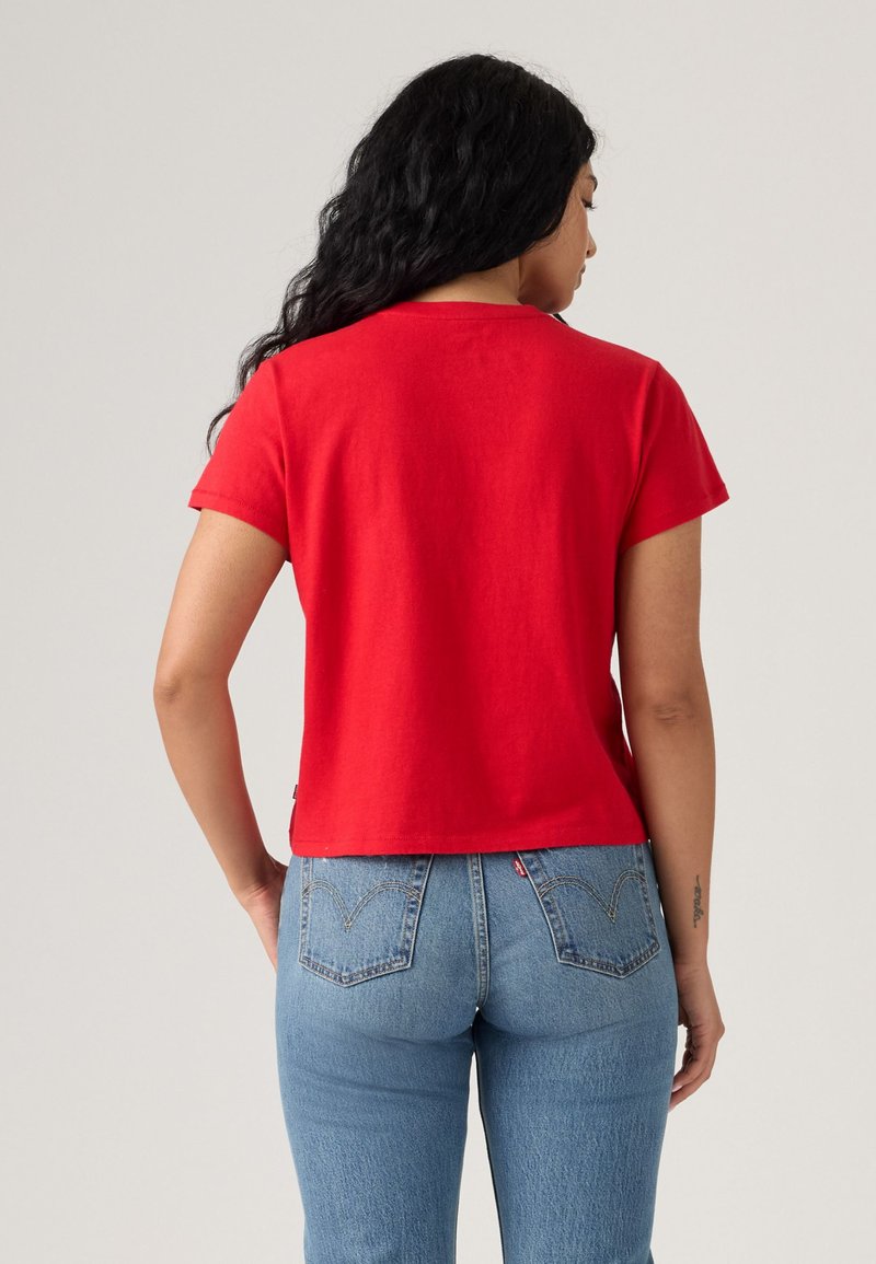 T-shirt en coton rouge à manches courtes, col rond et coupe droite, associée à un jean en denim bleu délavé avec des poches arrière.
