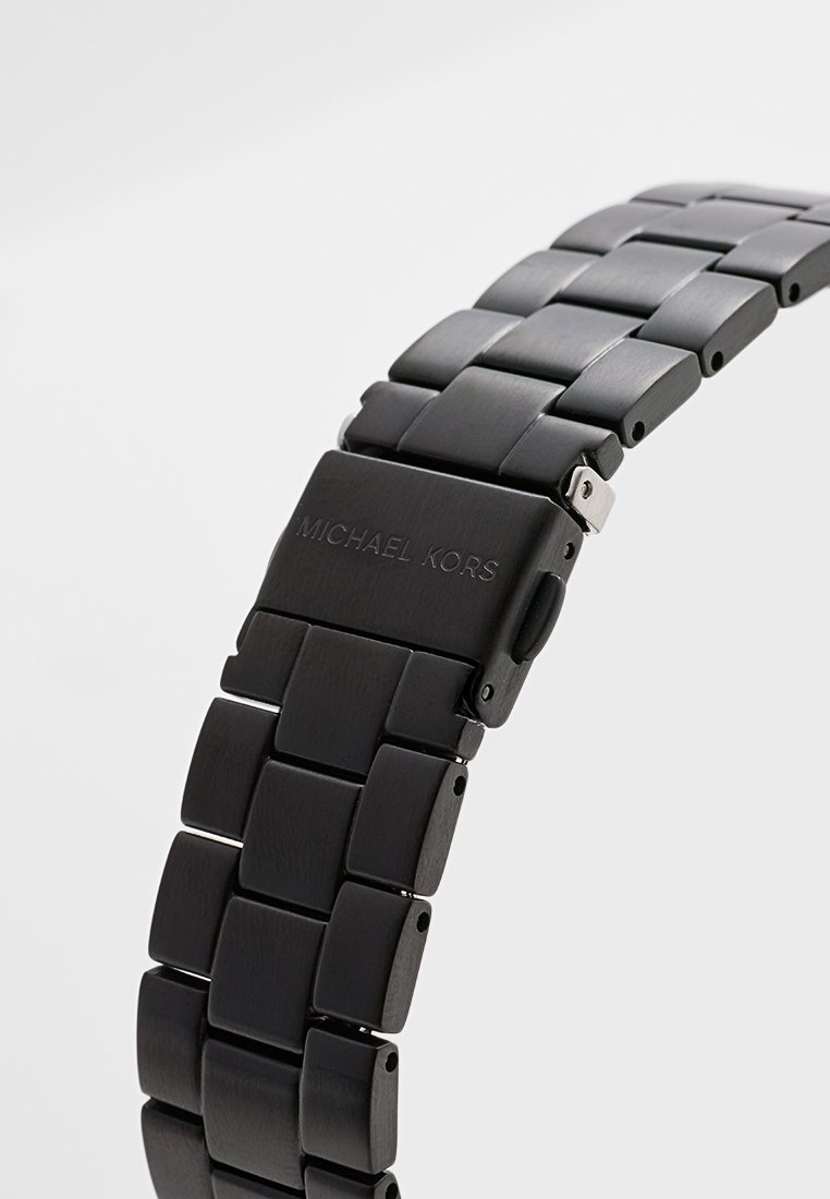 Bracelet de montre en acier inoxydable noir avec des maillons carrés et une finition mate. Doté d'un fermoir avec le nom de la marque en relief. Design simple et épuré.