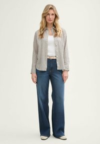 Een button-up shirt met een ruitenpatroon in grijs en wit. Een witte tanktop en lichtblauwe wijde jeans. Een beige riem. Witte sneakers.
