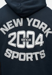 Μαύρο φούτερ με κουκούλα, με λευκά κεντημένα γράμματα που γράφουν "NEW YORK SPORTS since 2004" στην πλάτη κάτω από την κουκούλα.