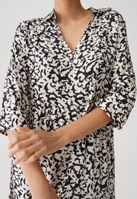 Long-sleeve dress in cream with abstract black pattern, featuring a V-neck, button front, and gathered waist for a relaxed fit.