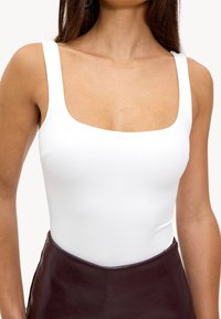 Witte aansluitende body met een vierkante halslijn en brede bandjes, gecombineerd met een hoog-geplooide, glanzende bordeaux leren rok.