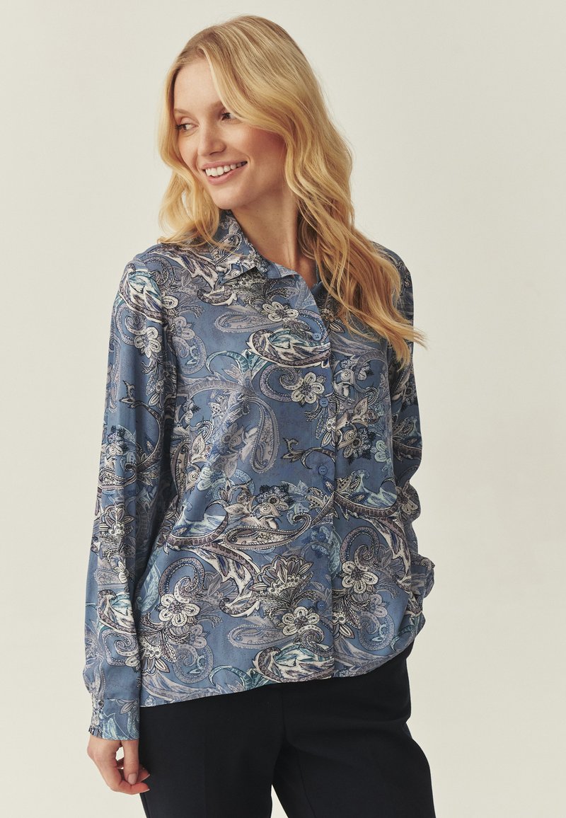 Blusa azul con estampado de cachemira, mangas largas, cuello y un ajuste relajado. La tela parece suave y ligera.