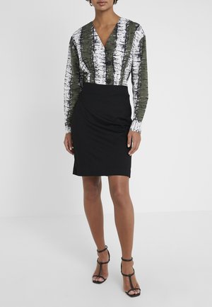 Femme portant un chemisier boutonné rayé vert et blanc, rentré dans une jupe noire longueur genou, avec des talons noirs à lanières.