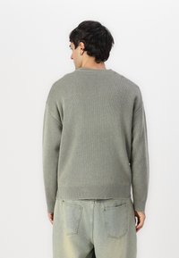 Világos zöld kötött pulóver kerek nyakkivágással, ejtett vállakkal és bordázott mandzsettákkal. Simább textúra, egyszerű design és laza szabás.