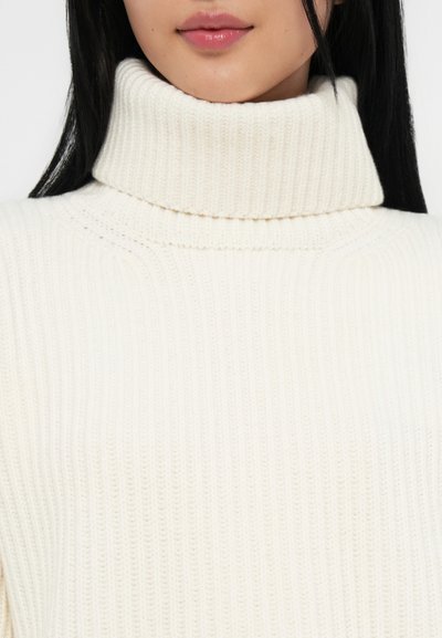 Krämfärgad, ribbad turtleneck-tröja med en tjock krage, som har vertikala ränder och en mjuk textur, lämplig för lager-på-lager användning eller som fristående plagg.