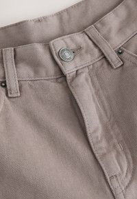 Jasnobrązowe bawełniane spodnie z zapięciem na guzik, paskiem z szlufkami i widoczną teksturowaną tkaniną o delikatnym połysku.