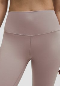 Różowe legginsy z wysokim stanem, wykonane z elastycznego materiału o gładkiej fakturze i kontrastowym przeszyciu wzdłuż szwów.