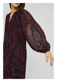 Långärmad klänning med djup V-ringning, prydd med ett vinrött blommönster på genomskinligt tyg och en samlad midja. Puffärmar betonar designen.