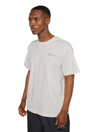 Jeune homme noir portant un t-shirt blanc à manches courtes avec un petit texte noir sur la poitrine et un short noir sur fond blanc.