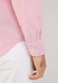 Rot-weißer gestreifter Langarmshirt mit Knopfmanschetten, aus glattem Material und leicht abgerundetem Saum. Sichtbares Knopfdetail an der Manschette.