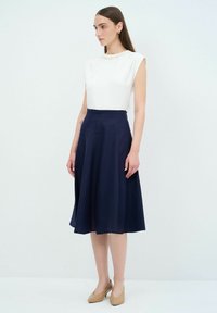 Top bianco senza maniche con scollo testurizzato, abbinato a una gonna A-line blu scuro. La modella indossa tacchi beige. Tessuto liscio e vestibilità su misura.