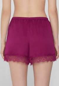 Magenta korte broek van gladde stof, met een kantafwerking aan de zoom. De tailleband is elastisch voor comfort. De achterkant laat het volledige ontwerp zien.