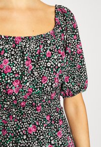 Gros plan d'une personne portant une robe noire avec un imprimé floral rose et blanc et des manches courtes bouffantes.