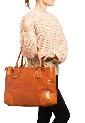 Borsa a mano in pelle marrone con texture liscia, accessori in oro, doppi manici e cuciture decorative. Persona che tiene la borsa in un contesto informale.