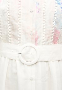 Λευκό φόρεμα από ύφασμα με φλοράλ λεπτομέρειες, διακοσμητική κάθετη δαντέλα, στρογγυλά κουμπιά καλυμμένα με ύφασμα και ζώνη με στρογγυλή αγκράφα.