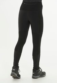 Leggings de sport noirs avec une taille haute, un tissu texturé, des poches latérales et des zones de genoux renforcées, associés à des chaussures de randonnée noires.
