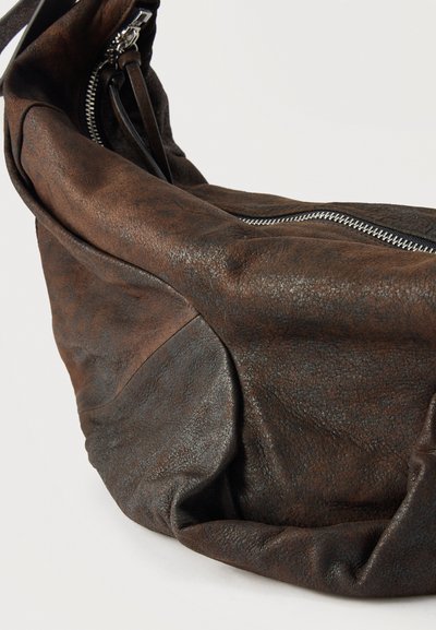 Σκούρο καφέ δερμάτινη τσάντα hobo με υφή, με ορατό ασημί φερμουάρ και ρυθμιζόμενο ιμάντα σε απλό λευκό φόντο.