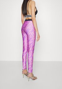 Lila blanka leggings med rosa textmönster. Matchas med en svart bandtopp och silverfärgade högklackade sandaler.