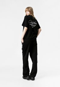 Camiseta negra de gran tamaño y pantalones de chándal negros. La camiseta tiene texto blanco en la parte posterior. Los pantalones de chándal tienen bolsillos laterales y un ajuste relajado.