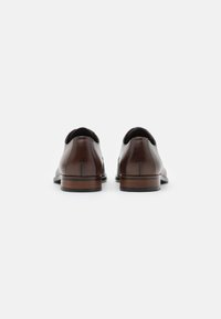 Chaussures de ville en cuir marron avec une finition lisse, bout arrondi et un talon en bois empilé. Détails de couture et éléments de design minimalistes.