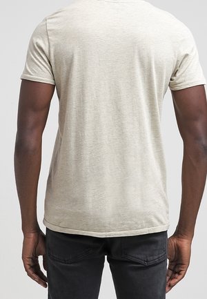 Short-sleeve beige t-shirt with a rounded neckline and a smooth texture, displayed from the back view, paired with dark jeans.