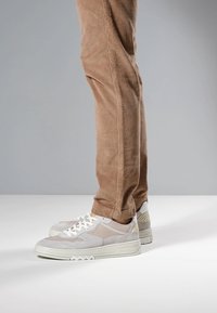 Baskets blanches et gris clair avec des détails en daim et en mesh, semelle en caoutchouc texturée et motif en zigzag. Associées à un pantalon en velours côtelé marron.