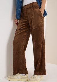 Bruine corduroy wijde broek met verticale ribbels, voorzien van voorzakken en een relaxte fit, gedragen met beige sneakers.
