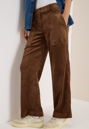 Bruine corduroy wijde broek met verticale ribbels, voorzien van voorzakken en een relaxte fit, gedragen met beige sneakers.