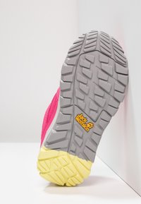 Trailová obuv s růžovým svrškem, šedou mezipodešví a žlutou podrážkou. Zoubkovaný vzorek pro trakci. Obsahuje logo "Jack Wolfskin".