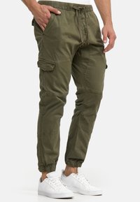Pantalon cargo vert olive avec poignets élastiques, taille à cordon et poches latérales. Confectionné dans un tissu doux et légèrement texturé.
