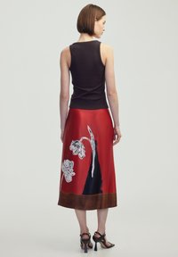 Rode satijnen rok met witte bloemenpatronen en een donkere zoom. Gepaard met een zwarte geribde tanktop en zwarte sandaaltjes met bandjes.