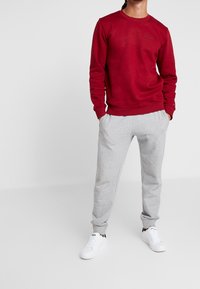 Felpa rossa girocollo abbinata a pantaloni della tuta grigi, caratterizzata da una vestibilità comoda. L'outfit è completato da sneaker bianche.