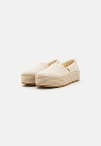 Scarpe slip-on beige con tomaia in tessuto intrecciato, suola in juta a pianta, e leggere dettagli testurizzati. Punta arrotondata e accento di branding minimo.