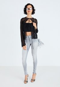 Črn prosojen top z naborki, nanešen čez črn crop top; v paru z svetlo sivo ozkimi džinsami in kovinskimi natikači z odprtimi prsti. Srebrna torbica z resicami.