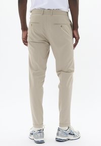 Pantalon beige avec une coupe slim, une taille structurée et deux poches arrière. Assorti à des chaussures de sport argentées et bleues.