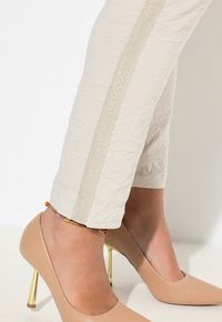 I pantaloni beige a culotte presentano una texture stropicciata e una sottile striscia dorata lungo i lati. Abbinati a tacchi alti color nude con dettagli dorati sul tacco.