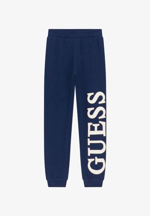 Marineblaue Jogginghose mit elastischem Bund und Bündchen, mit einem großen weißen "GUESS"-Logo, das das linke Bein hinuntergedruckt ist. Glatte Textur.