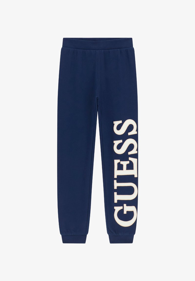 Donkerblauwe joggingbroek met elastische tailleband en boorden, met een groot wit "GUESS" logo gedrukt aan de linkerkant van het been. Gladde textuur.