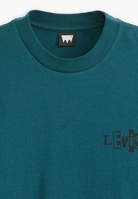 Tricou din bumbac de culoare teal, cu guler rotund, mâneci scurte și un print grafic negru cu cuvântul "Levi's" în partea stângă jos.