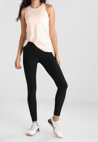 Lys ferskenfarvet tanktop med rund halsudskæring, sorte leggings og hvide sneakers med pink og sorte accenter. Glat stof og tætsiddende design.