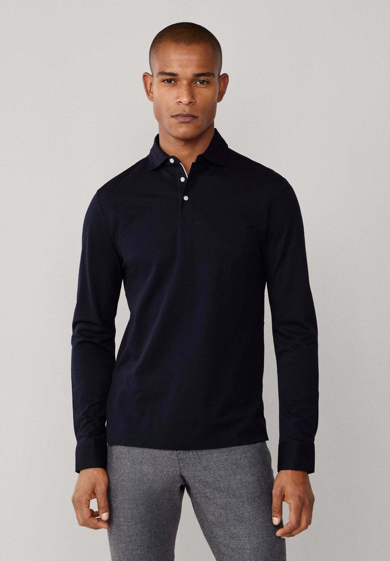 Mornarska polo majica dugih rukava s ovratnikom, s plastičnim kopčanjem na tri gumba i glatkom teksturom tkanine. Uparena s sivim hlačama.