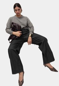 Grijze gebreide trui, wijde donkere spijkerbroek met contrasterende stiksels, leopardprint hakken met puntige neuzen, met een bordeauxkleurige tas.