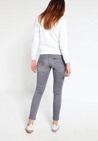 Jeans ajustados grises de denim, con un diseño sin costuras, bolsillos traseros y una cintura de altura media, combinados con un suéter blanco y zapatillas.