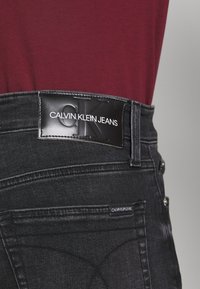 Czarne jeansy z denimu z skórzaną naszywką z logo Calvin Klein na pasku, wyraźnymi szwami przy kieszeniach oraz delikatnym efektem sprania.