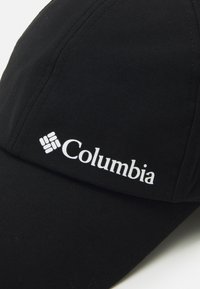 Czarna czapka z tkaniny z zakrzywionym daszkiem. Posiada wyraźne białe logo "Columbia" z przodu. Gładka tekstura z minimalnym przeszyciem.